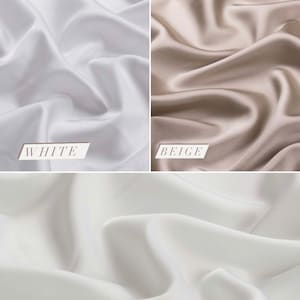 May include: Three swatches of fabric in different shades of white: white, beige, and light ivory. The fabric is smooth and silky.