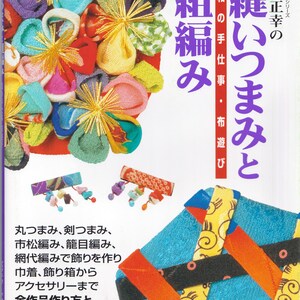 Könnte beinhalten: Ein Buch mit dem Titel "Nähen von kleinen Falten und Knoten: Japanisches Handwerk" mit einem violetten Einband und bunten Stoffmustern auf der Vorderseite. Das Buch enthält Anleitungen zum Herstellen verschiedener Handarbeiten, darunter kleine Stoffblumen, Beutel und Accessoires.