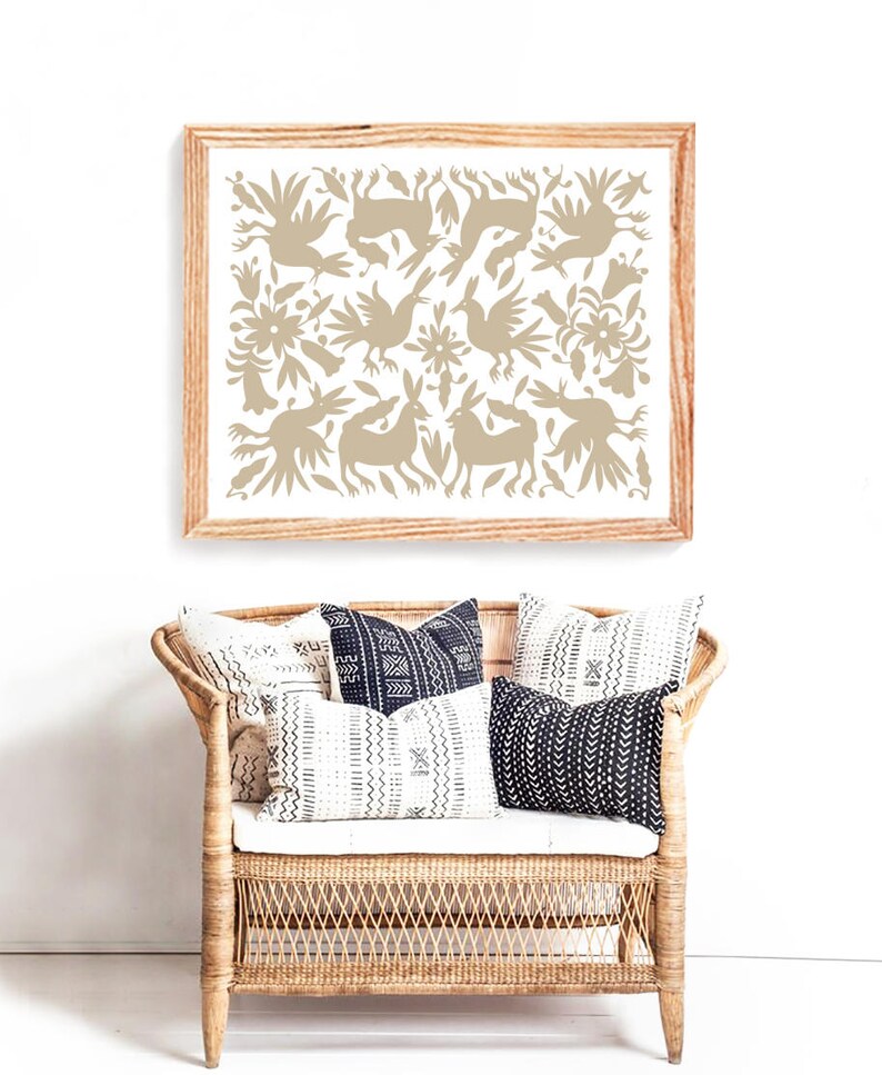 Op de afbeelding: Een ingelijst print met een beige ontwerp van gestileerde vogels, konijnen en bloemen op een witte achtergrond. De print hangt aan een witte muur boven een rieten bank met zwart-witte gepatroneerde kussens.