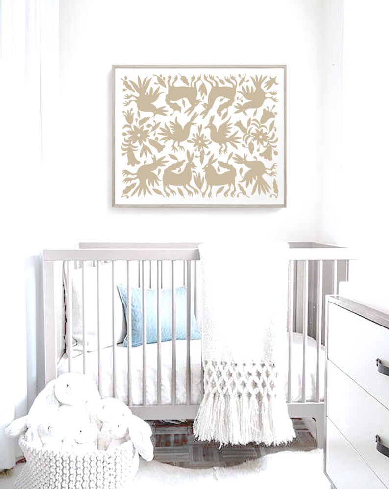 Op de afbeelding: Een wit babybedje met een wit gehaakt dekentje en een witte rieten mand gevuld met knuffels. Een beige ingelijst print met een bruin volkskunstontwerp hangt aan de muur boven het babybedje.