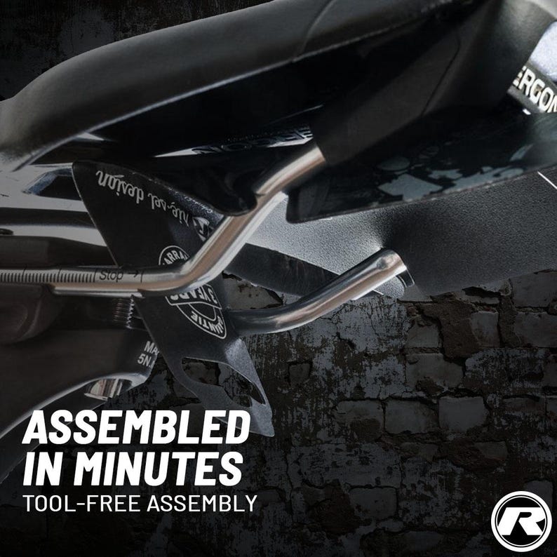 May include: Close-up of a black bicycle seat with silver metal supports. The seat has the text "ASSEMBLED IN MINUTES TOOL-FREE ASSEMBLY" in white. The brand logo is in the bottom right corner.