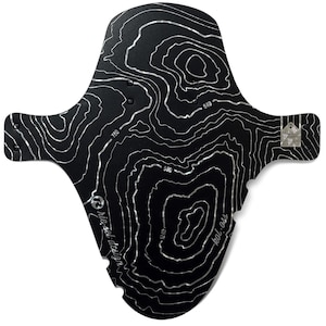 May include: Black bicycle fender with a topographic map design in silver. The fender has a unique shape with extended side flaps and a rear mounting tab. The text "rie:sel design" and "kol:ass" are visible. The fender is labeled "MADE IN GERMANY ORIGINAL".