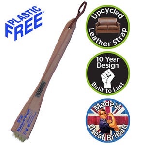 Puede incluir: Un cepillo de zapatos de madera con mango marr&oacute;n claro y cabezal de cepillo. El cepillo tiene una correa de cuero para colgarlo. El texto en el cepillo dice "Massive-Brush". El texto adicional incluye "Plastic Free", "Upcycled Leather Strap", "10 Year Design Built to Last" y "Made in Great Britain".