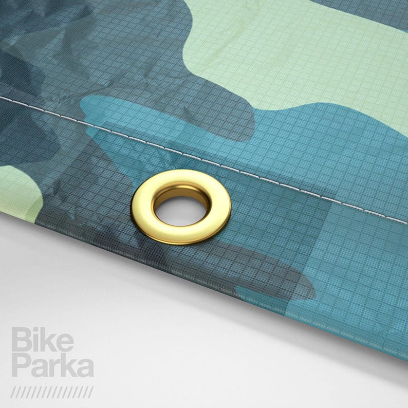 May include: Close-up of a section of a camouflage-patterned fabric in shades of blue and green. A gold-colored grommet is visible near the edge. The text "Bike Parka" is printed in white on the lower left corner.