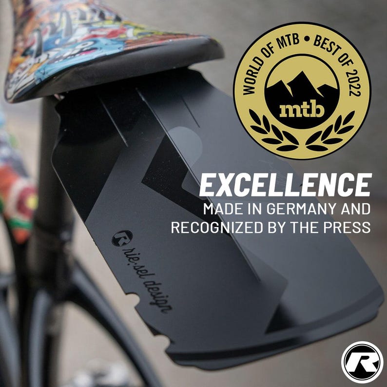 May include: Black bicycle fender with the text "EXCELLENCE MADE IN GERMANY AND RECOGNIZED BY THE PRESS". The fender is attached to a bicycle. A gold emblem reads "WORLD OF MTB BEST OF 2022". The brand logo is visible.