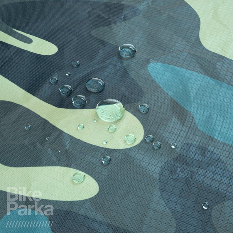 May include: Close-up of a camouflage pattern fabric with water droplets. The fabric features a mix of blue, green, and white shapes. The words "Bike Parka" are visible in the lower left corner.
