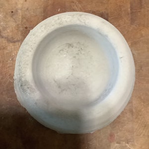 Peut inclure: Un mortier et pilon circulaires gris clair. Le mortier a un large bol peu profond avec une surface textur&eacute;e. Le pilon n'est pas visible. Le mortier est fait d'un mat&eacute;riau semblable &agrave; de la pierre et repose sur une surface en bois.
