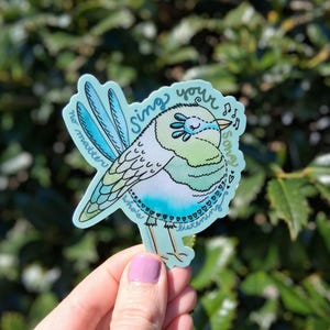 May include: A blue and green watercolor sticker of a bird singing with the text "Sing your song no matter who is listening".