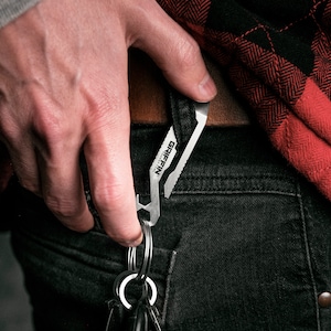 May include: A silver multi-tool keychain with the text "GRIFFIN" and "ULTIMATE TOOL" on it. The keychain is attached to a set of keys and is being held in a person's hand.