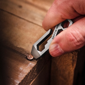 May include: A silver multi-tool with the text "GRIFFIN MINI" on it. The tool is being used to remove a nail from a piece of wood.
