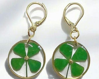 Peut inclure: Une paire de boucles d'oreilles en or avec un trèfle à quatre feuilles pressé dans de la résine transparente. Le trèfle est vert avec un centre doré.
