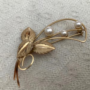 May include: A gold-toned brooch with a floral design and three faux pearl accents.