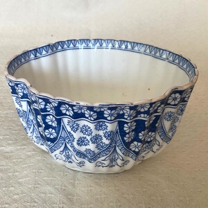Peut inclure: Un bol en céramique blanc et bleu avec un bord festonné. Le bol présente un motif floral détaillé en bleu sur un fond blanc. Le motif comprend une bande de petites fleurs et des éléments décoratifs.