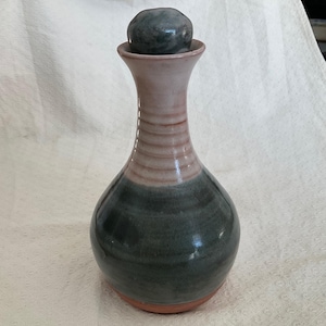 May include: A ceramic bottle with a green and pink glaze. The bottle has a round body and a tall neck with a round stopper.