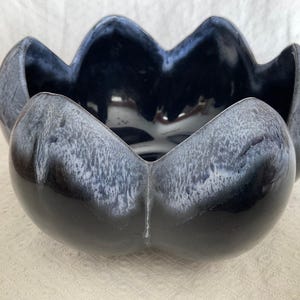 May include: A dark blue ceramic bowl with a distinctive, scalloped edge design. The bowl has a glossy finish with a gradient effect, transitioning from a deep blue to a lighter, almost white, colour near the edges. A decorative piece.