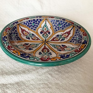 May include: Oval ceramic serving dish with a hand-painted floral design. The dish has a teal green rim and a central pattern in yellow, blue, red, and teal. The intricate design is reminiscent of traditional Moroccan pottery.