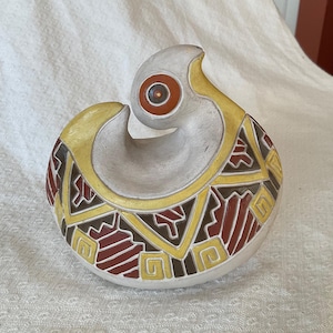 May include: A ceramic sculpture with a rounded base and a curved, open top. The sculpture features a grey base with yellow, brown, and red geometric patterns. The top has a circular design with a red centre and a yellow outline.
