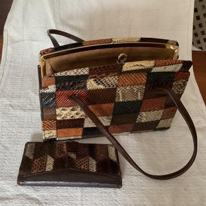 May include: A vintage handbag and matching wallet set. The bag has a patchwork design in shades of brown, tan, and black. The wallet has a similar pattern. Both items have brown leather handles and trim. The bag is open, revealing a tan interior.
