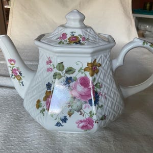 May include: White teapot with a floral pattern and a woven design. The teapot has a lid and a handle.
