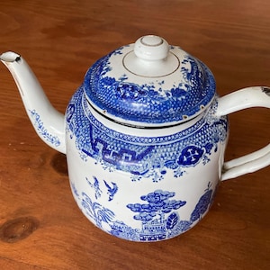 May include: A white and blue ceramic teapot with a lid. The teapot has a blue and white Chinoiserie design with landscape and bird motifs. The handle and spout are white. The lid has a white knob with gold trim.