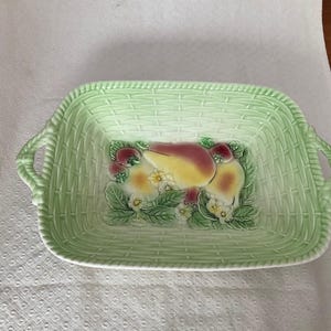May include: A rectangular, pale green ceramic serving dish with a basket weave pattern. The dish has two handles and a central fruit and floral design with pears, strawberries, and flowers.
