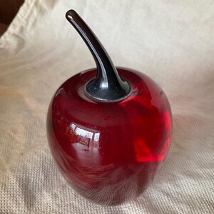 May include: A red glass cherry with a black glass stem. The cherry is a decorative object.