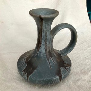 May include: A blue ceramic candle holder with a brown glaze and a handle. The holder has a wide base and a narrow neck.