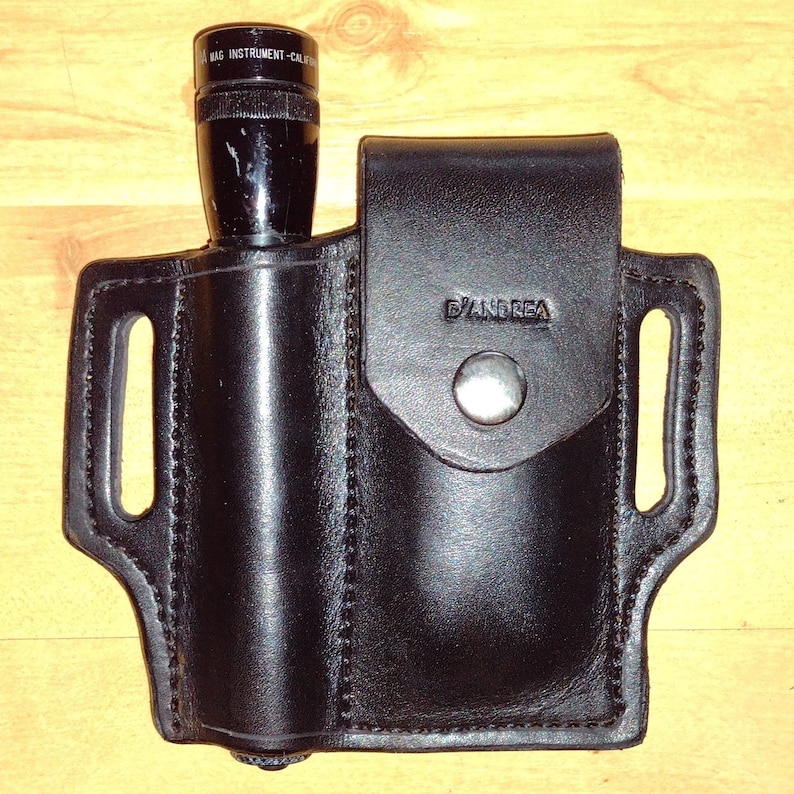 May include: Black leather holster with a snap closure and the text "D'Andrea" embossed on the front. A black flashlight with the text "MAG INSTRUMENT - CAL"