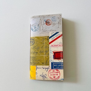 May include: A handmade journal with a collage of vintage ephemera. The cover features postage stamps, handwritten letters, and airmail labels in red, blue, and yellow. The journal is stitched together with yellow thread.