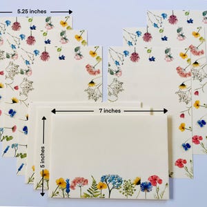 May include: Set of eight floral note cards with white envelopes. The cards are 5 inches by 7 inches and feature a pressed flower design with pink, yellow, blue, and green flowers. The cards are perfect for writing thank you notes, birthday cards, or any other occasion.