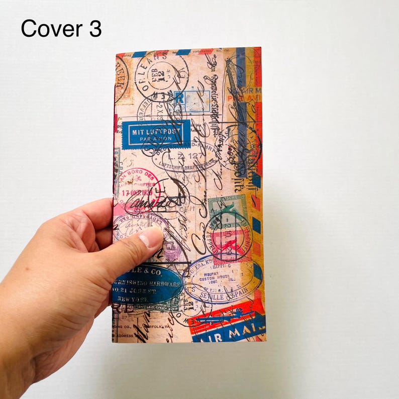 May include: A rectangular notebook cover featuring a vintage airmail theme with a beige background, various black ink postmarks, stamps, and handwritten script. The design includes blue, red, and yellow accents with text such as MIT LUFTPOST.