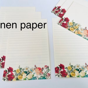 Puede incluir: Una pila de papel rayado con un borde floral. El papel es de color crema y tiene una textura de lino. El borde presenta flores rojas, rosas, amarillas y blancas.