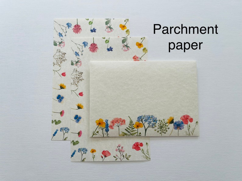 May include: Three sheets of parchment paper with a floral design. The paper is cream colored with a border of blue, yellow, pink, and green flowers. The text "Parchment paper" is printed in black at the top of the image.
