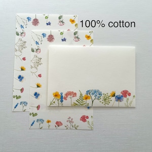 May include: Three sheets of stationery paper with a floral design. The top sheet is blank, the middle sheet has a scattered floral design, and the bottom sheet has a floral border. The text "100% cotton" is printed on the top of the image.