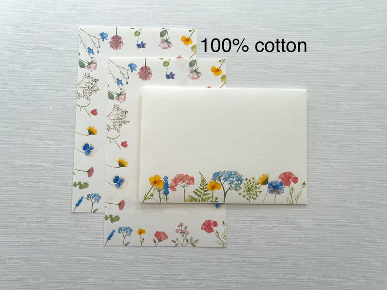 May include: Three sheets of stationery paper with a floral design. The top sheet is blank, the middle sheet has a scattered floral design, and the bottom sheet has a floral border. The text "100% cotton" is printed on the top of the image.