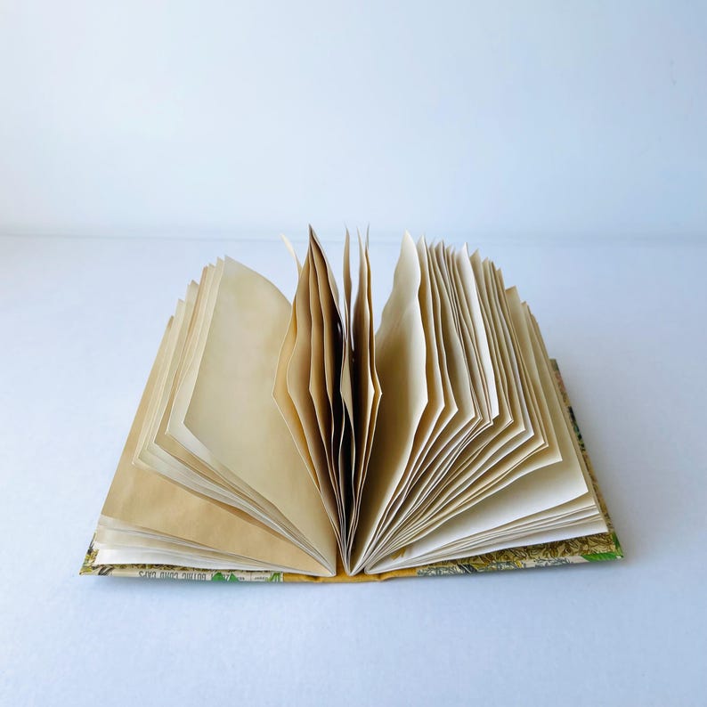 May include: An open book with blank pages and a patterned cover. The cover features a floral design with green, brown, and yellow colors.