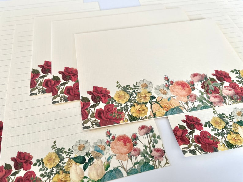 Puede incluir: Conjunto de papeler&iacute;a con un borde floral de rosas rojas, rosas y amarillas, junto con hojas verdes y flores blancas. El papel tiene espacio de escritura rayado.