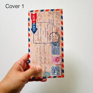 May include: A rectangular notebook cover featuring a vintage airmail envelope design with red and blue striped borders. The cover displays printed postage stamps, postmarks, and handwritten script text including Air Mail, Washington, and 1934.
