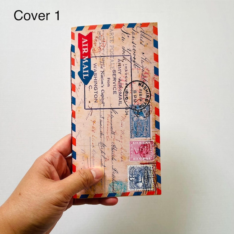 May include: A rectangular notebook cover featuring a vintage airmail envelope design with red and blue striped borders. The cover displays printed postage stamps, postmarks, and handwritten script text including Air Mail, Washington, and 1934.