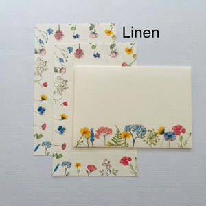 May include: Three sheets of stationery with a floral design. The top sheet has a border of small flowers, the middle sheet has a scattered floral design, and the bottom sheet has a border of larger flowers. The text "Linen" is printed in black at the top of the image.