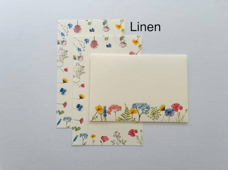 May include: Three sheets of stationery with a floral design. The top sheet has a border of small flowers, the middle sheet has a scattered floral design, and the bottom sheet has a border of larger flowers. The text "Linen" is printed in black at the top of the image.