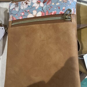 May include: A brown faux leather crossbody bag with a zippered pocket and a floral print flap. The bag has a long adjustable strap.