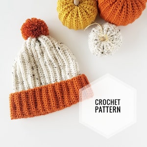 Può includere: Un berretto a maglia bianco e arancione con un pon pon bianco in cima. Il berretto ha una trama a coste e un bordo arancione a contrasto. Il testo "CROCHET PATTERN" è visibile nell'immagine.