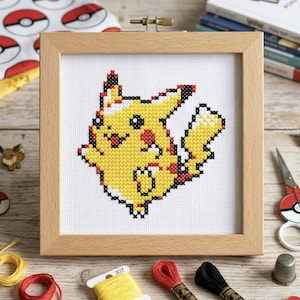 Może przedstawiać: Kwadratowa drewniana ramka do haftowania zawierająca wzór haftu krzyżykowego przedstawiający żółtego Pikachu z czerwonymi policzkami, czarnymi końcówkami uszu i ogonem w kształcie błyskawicy, wyszyty na białej tkaninie z czarnym konturem.