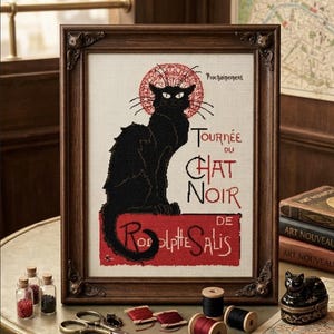 May include: A framed cross-stitch embroidery featuring a black cat sitting on a red rectangular base. The text reads "Prochainement", "Tournée du Chat Noir", and "de Rodolphe Salis". The dark wooden frame has small cat-shaped corner accents.