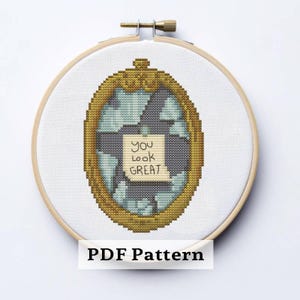 May include: A cross-stitch design in a wooden embroidery hoop. The design features a gold-framed mirror with a shattered appearance, and a note that reads "You look GREAT." The words "PDF Pattern" are at the bottom.