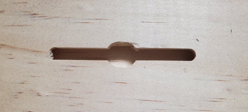 K&ouml;nnte beinhalten: Nahaufnahme einer hellen Holzoberfl&auml;che mit einem rechteckigen Ausschnitt. Das Loch hat eine abgerundete Kante und ist mittig auf der Oberfl&auml;che angeordnet.