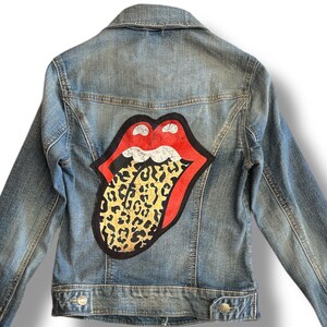 Könnte beinhalten: Eine blaue Jeansjacke mit einem großen roten und schwarzen Zungen-Patch mit Leopardenmuster.