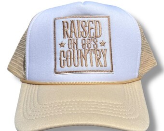 May include: A white and beige trucker hat with a gold embroidered patch that says "RAISED ON 90's COUNTRY" with stars on either side of "90's".
