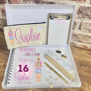 May include: A white gift box containing a personalized pencil case, a spiral-bound notebook, a clipboard, and stationery. The pencil case and notebook feature the name "Sophie" and a cartoon illustration. The notebook reads "Memories of the Fun I Had The Year I was 16 Sophie 30.04.24".